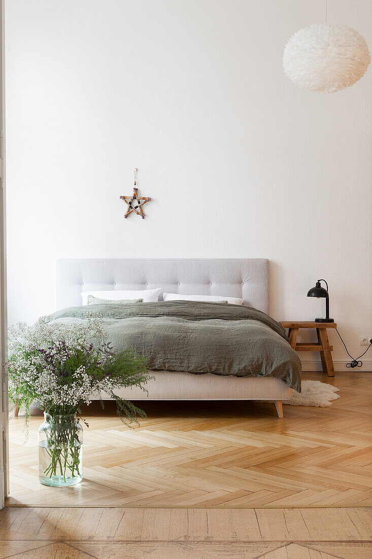 Doppelbett und Glasvase mit Gartenblumen in minimalistischem Schlafzimmer
