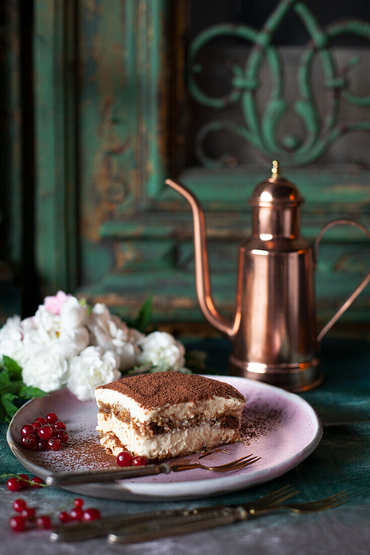 A slice of tiramisu garnished with redcurrants and flowers