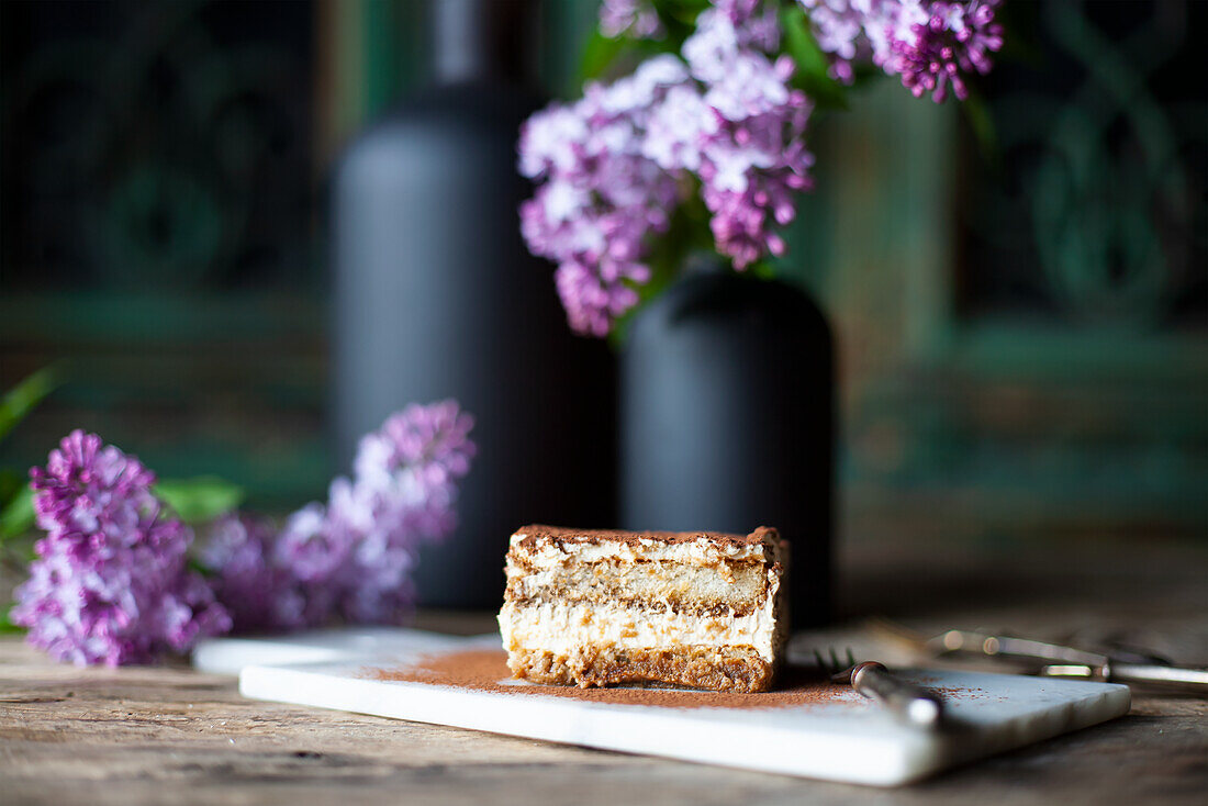 Ein Stück Tiramisu im Hintergrund Fliederblüten