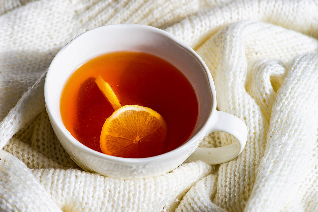 Cup of hot tea with lemon and white knitted sweater as a winter concept