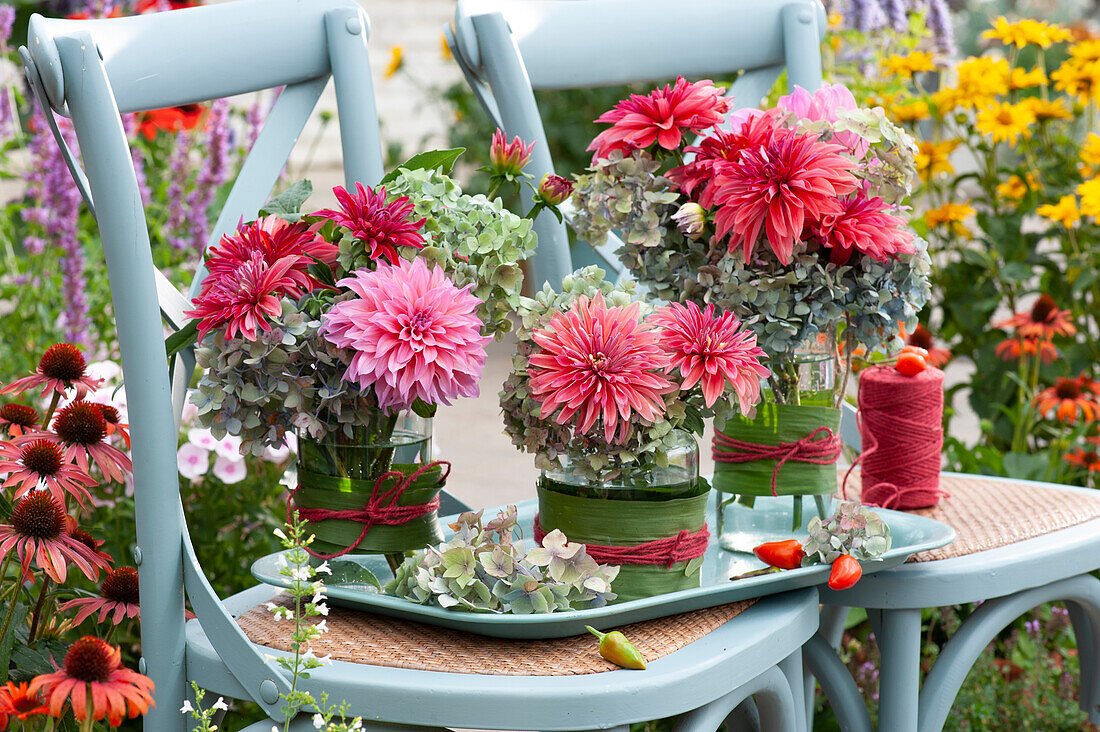 Sträuße mit Dahlien und Hortensienblüten in mit Blättern umwickelten Gläsern