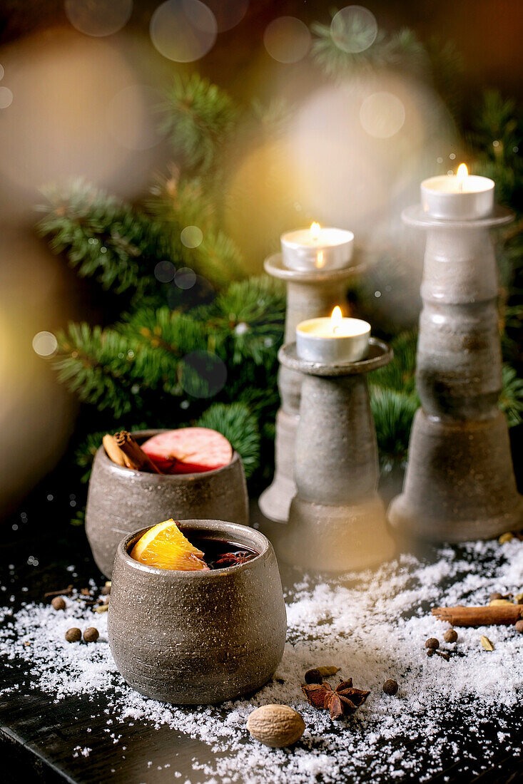 Glühwein in Keramikbechern mit Gewürzen, Orangen- und Apfelscheibe und Weihnachtsdeko
