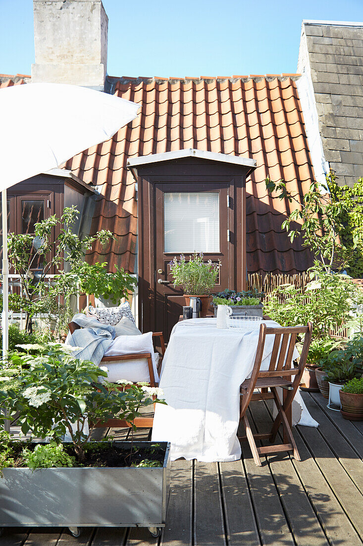 Table with white tablecloth, chair and bench on roof terrace with planters