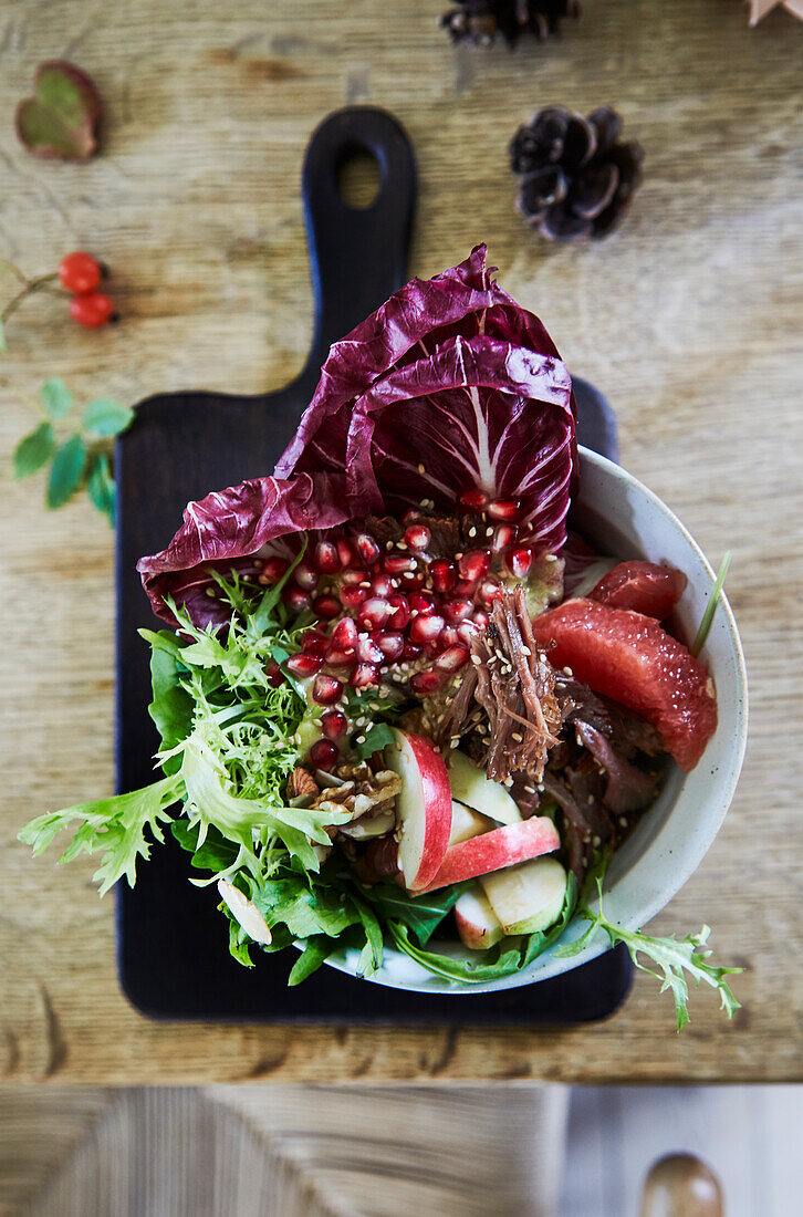 Salat mit Radicchio, Granatapfelkernen und Apfelspalten in Schüssel auf Holztisch