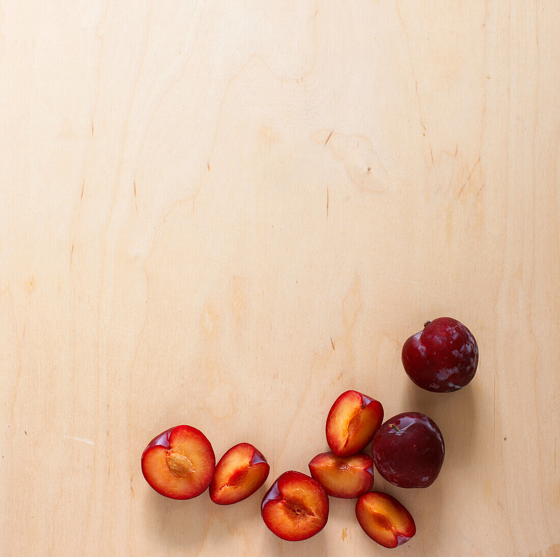 Whole, cored and sliced plums on wooden surface