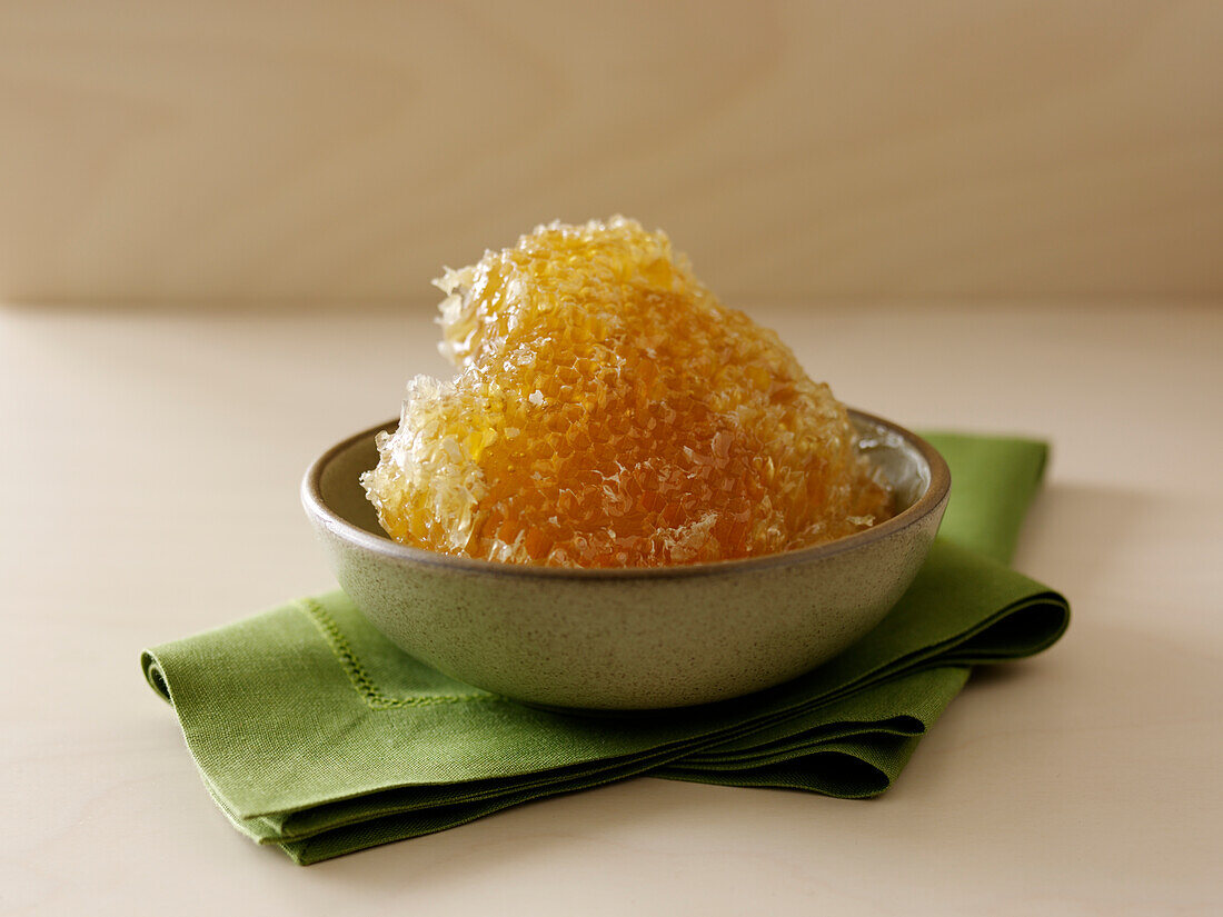 Honeycomb covered in honey in a bowl on a green napkin