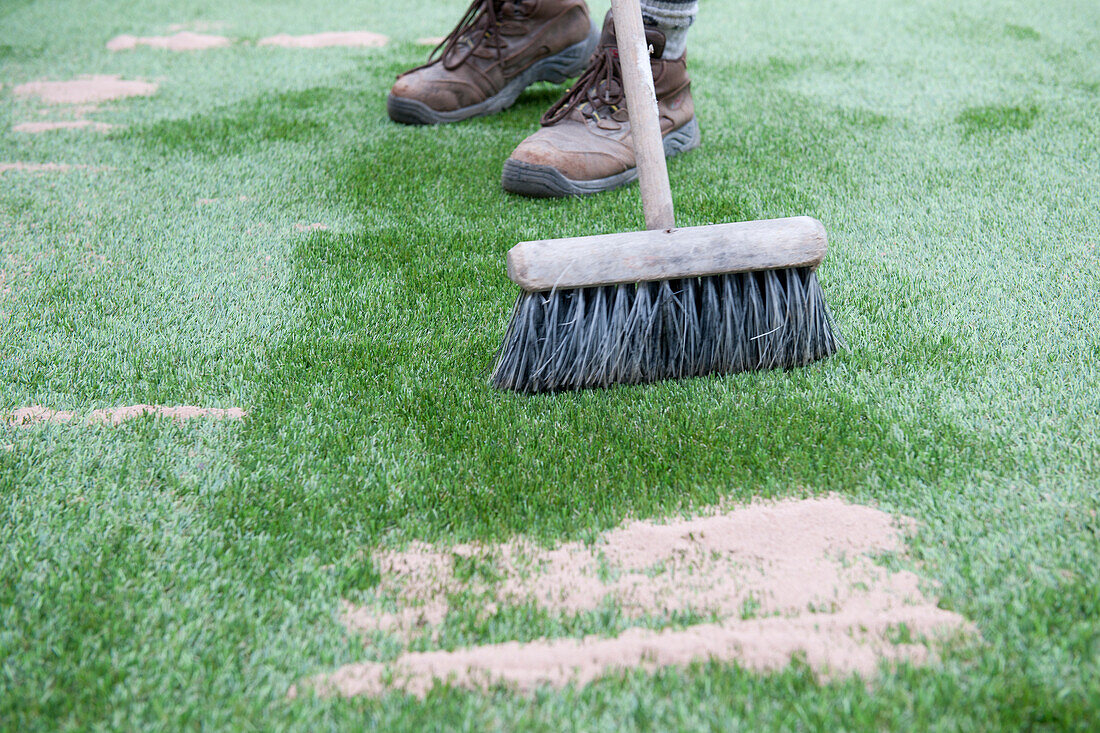 Brushing silica sand into the surface of artificial turf