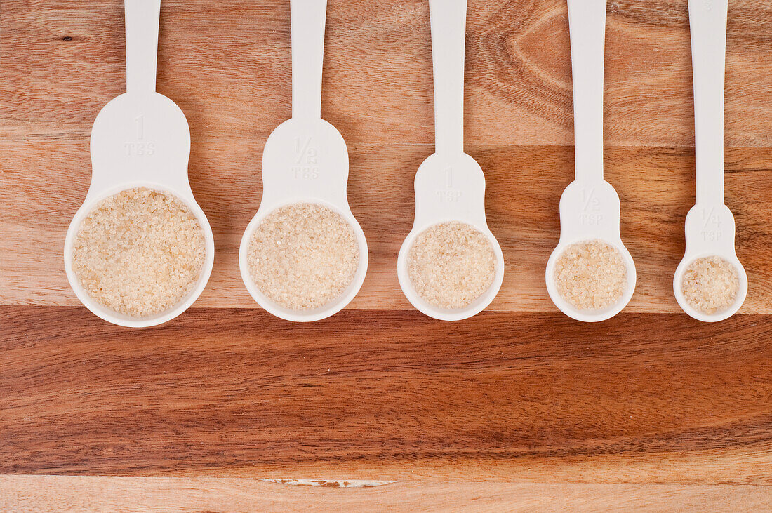 Row of plastic measuring spoons filled with brown sugar