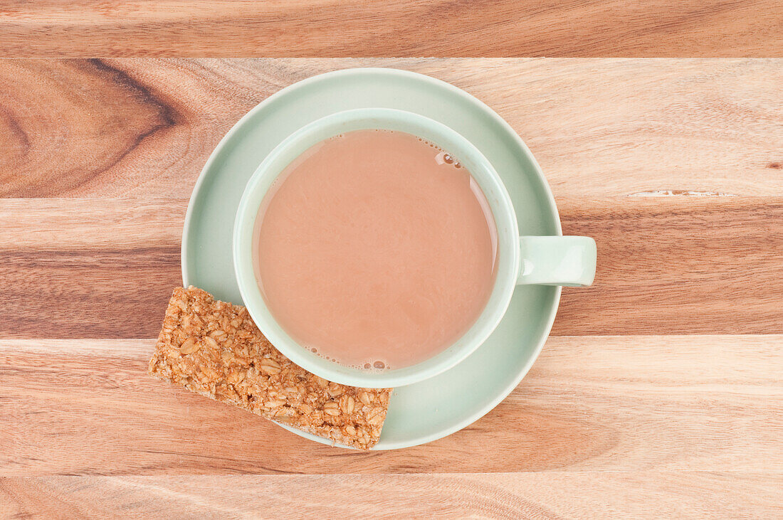 Cup of milky tea with oat biscuit on saucer