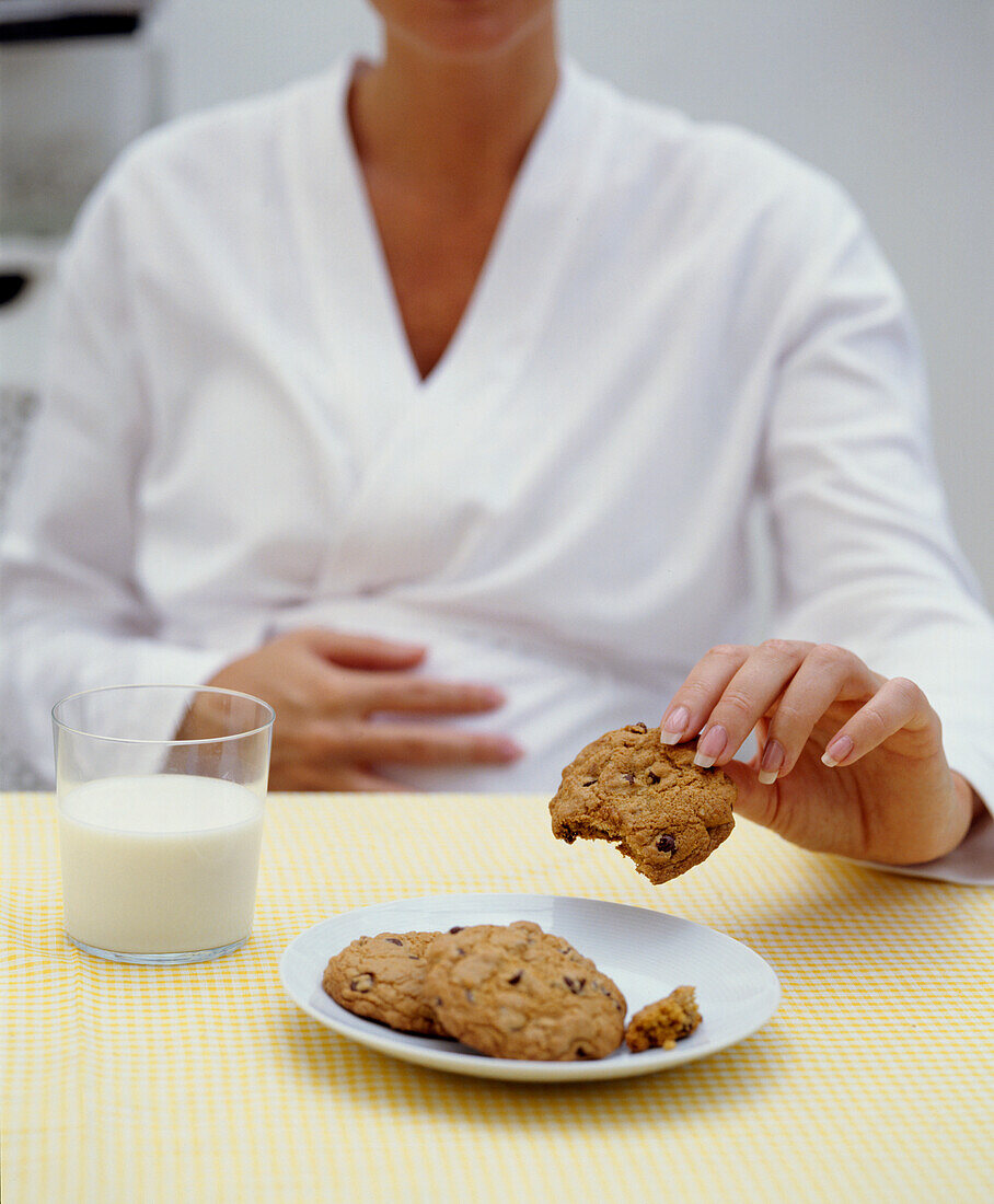 Pregnant woman touching bump and holding cookie