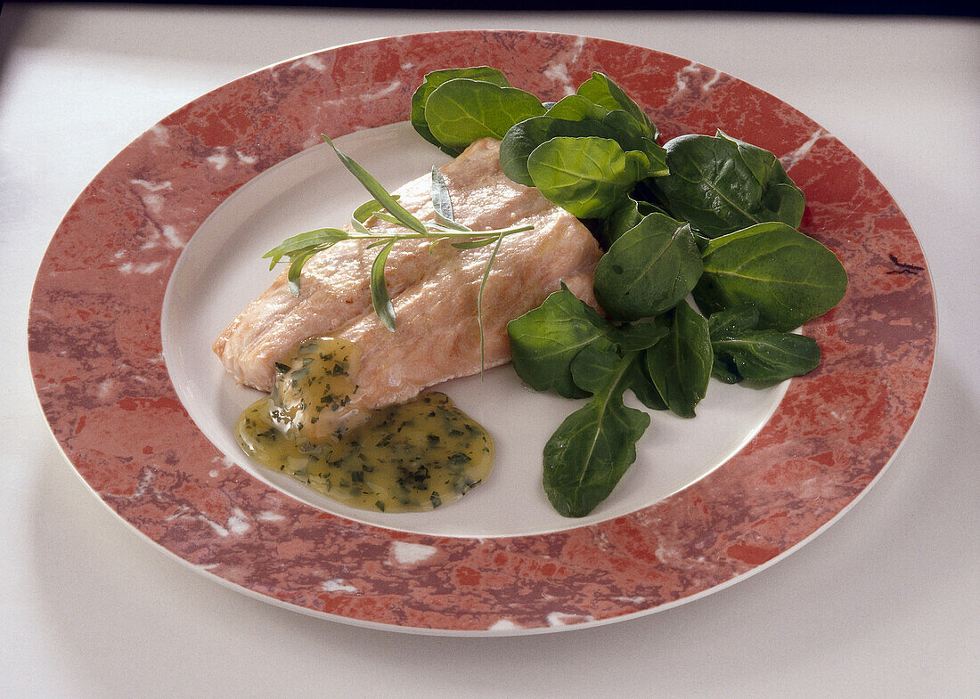 Salmon fillet served with sauce and rocket leaf salad