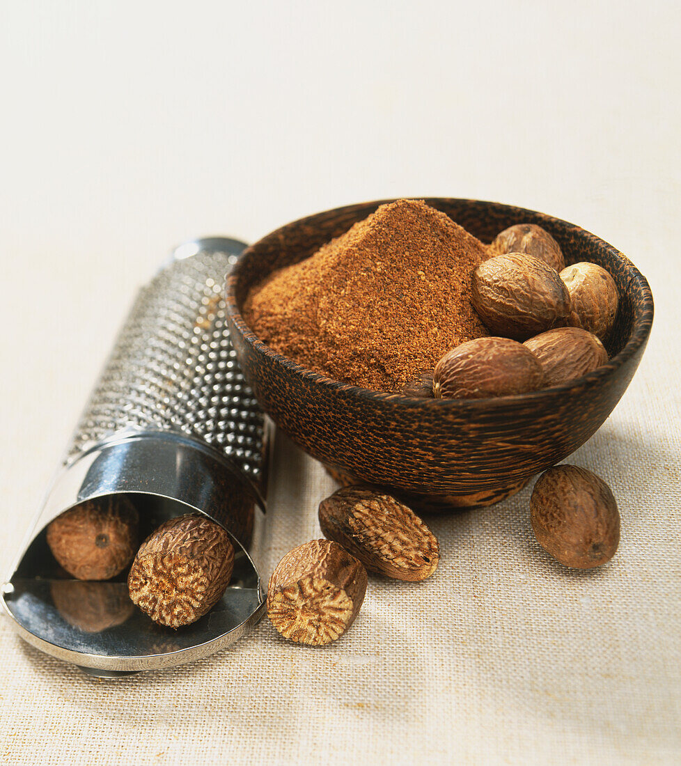 Whole nutmeg kernels and ground nutmeg in wooden bowl
