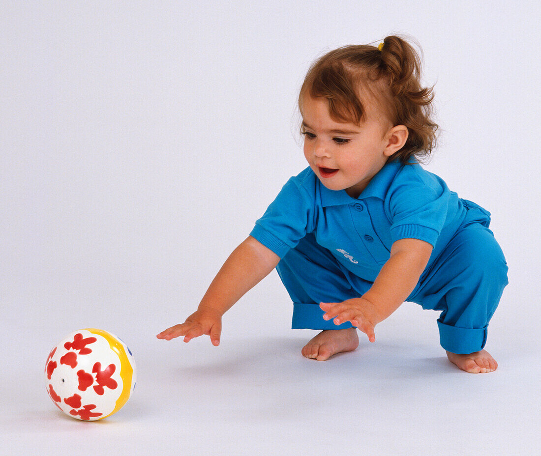 Squatting toddler reaching forward to touch coloured ball