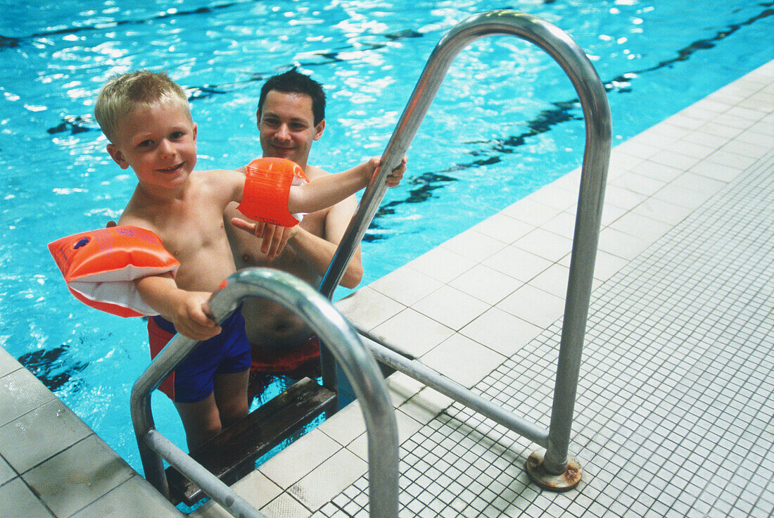 Boy wearing water wings at a swimming pool with father