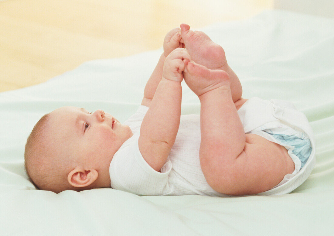 Baby lying on back and clutching toes with hands