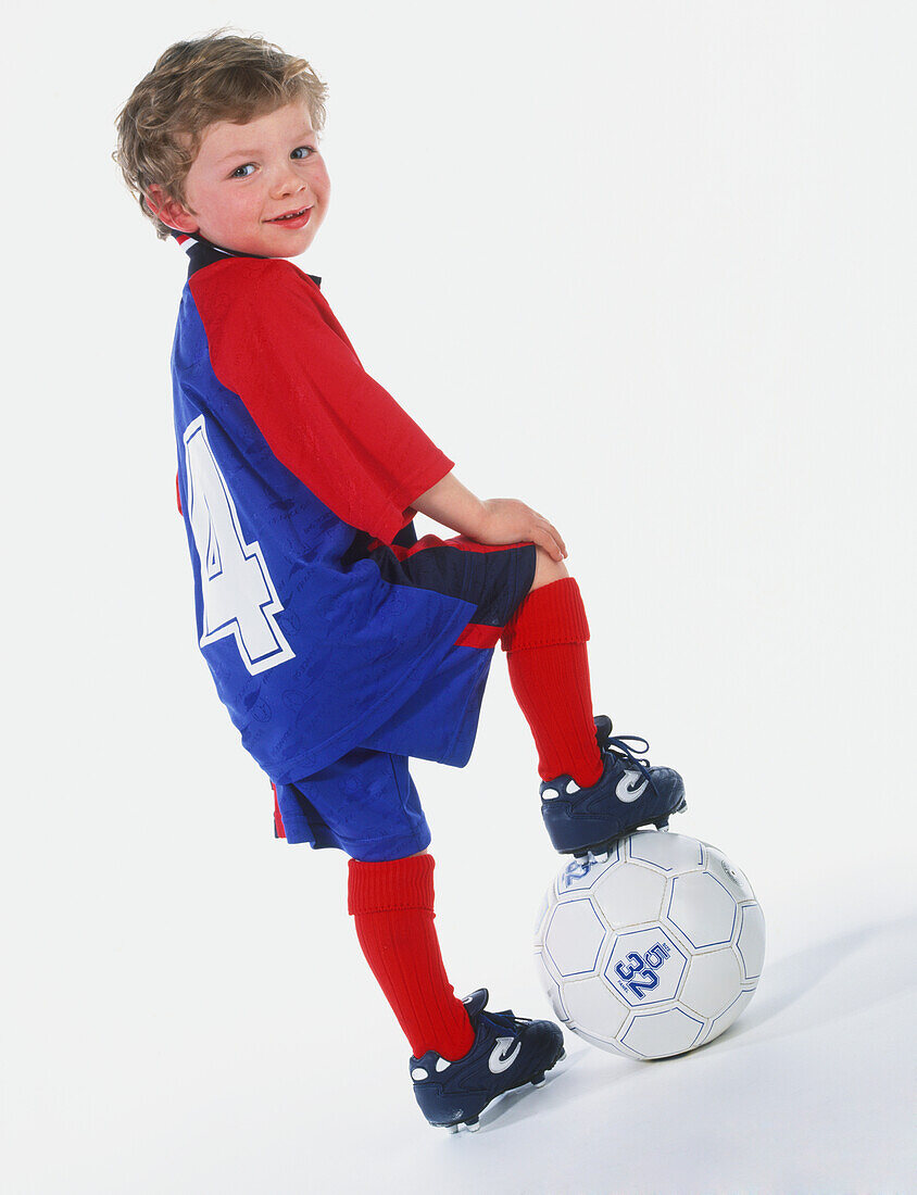 Boy in football clothes resting his right foot on a ball