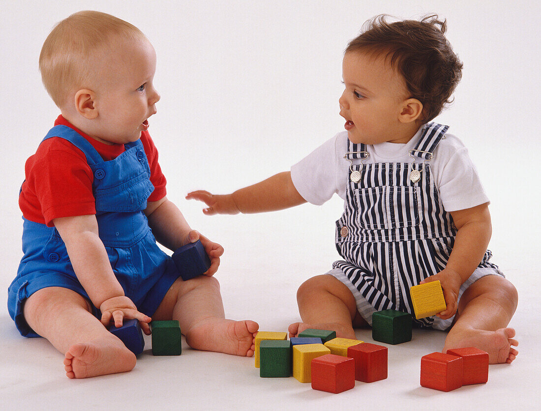 Two babies playing with brightly coloured wooden blocks