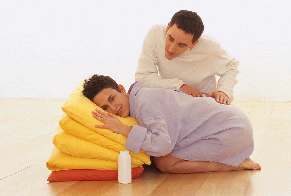 Man rubbing back of a pregnant woman resting on cushions