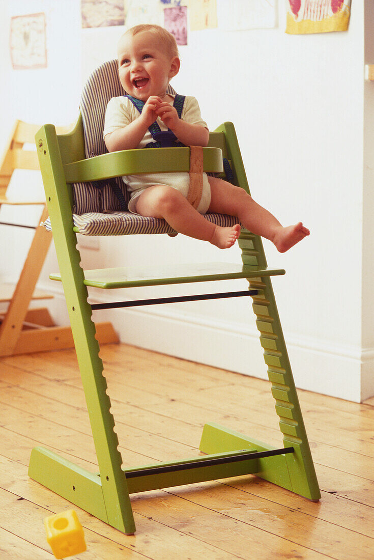 Laughing blonde baby sitting in a green highchair