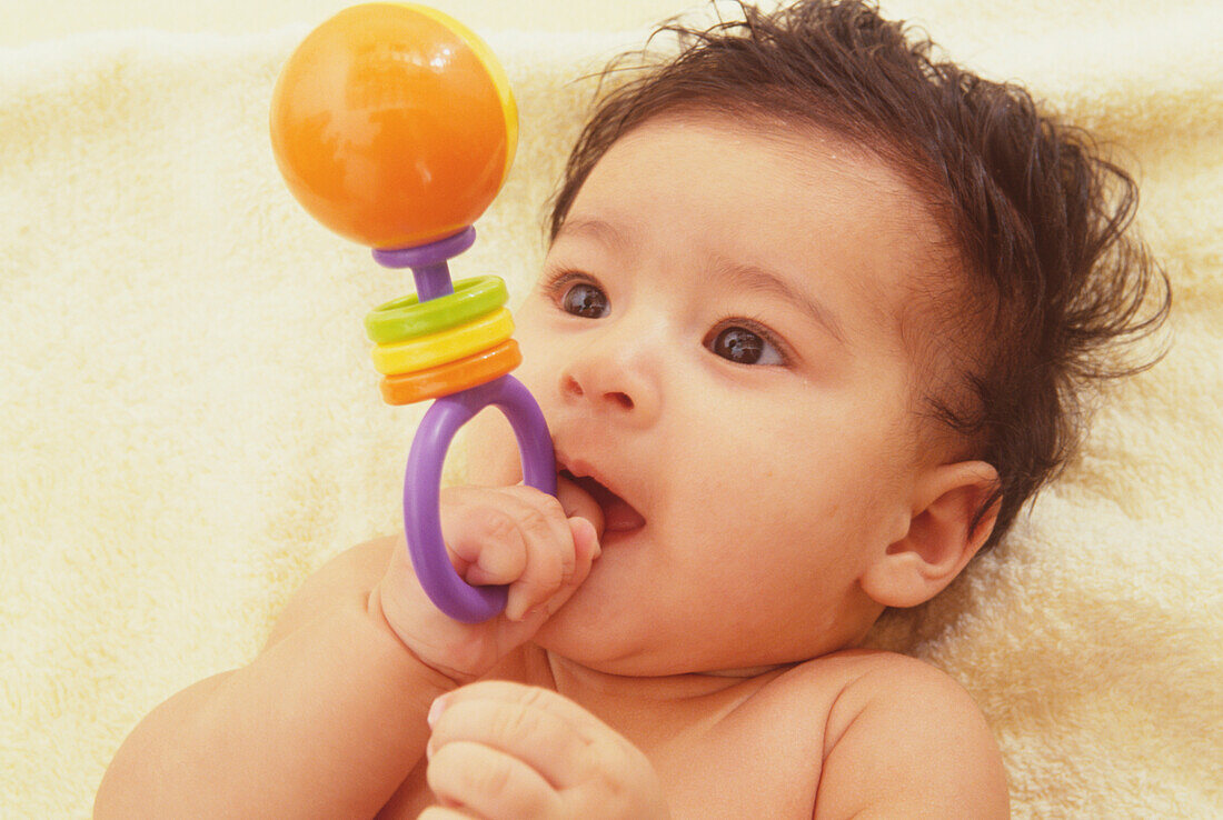 Baby pressing handle of a plastic rattle against her lips