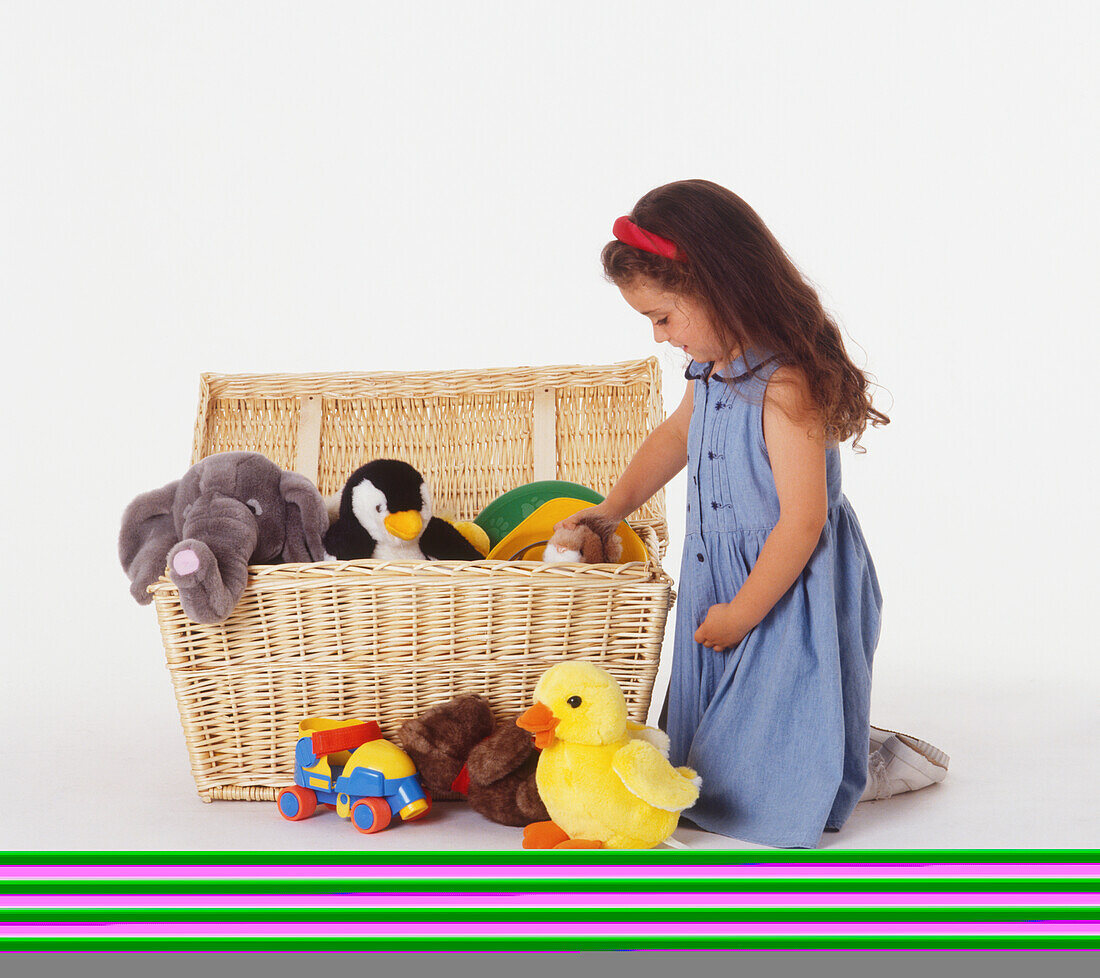Girl kneeling putting toys in a wicker box