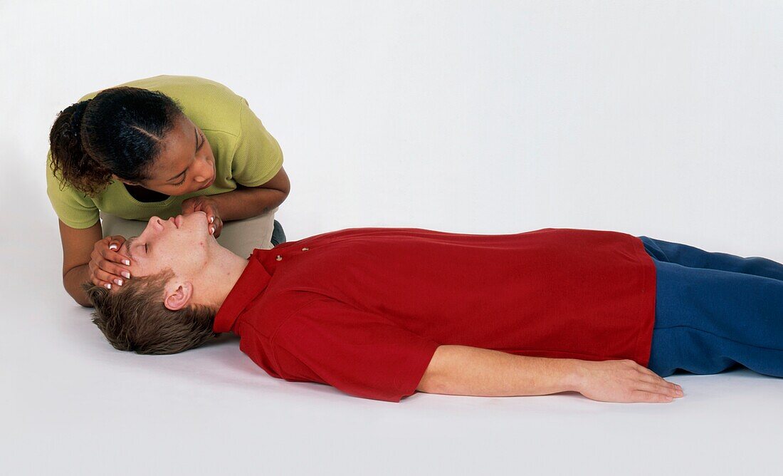 Woman kneeling and checking the breathing of a man on floor