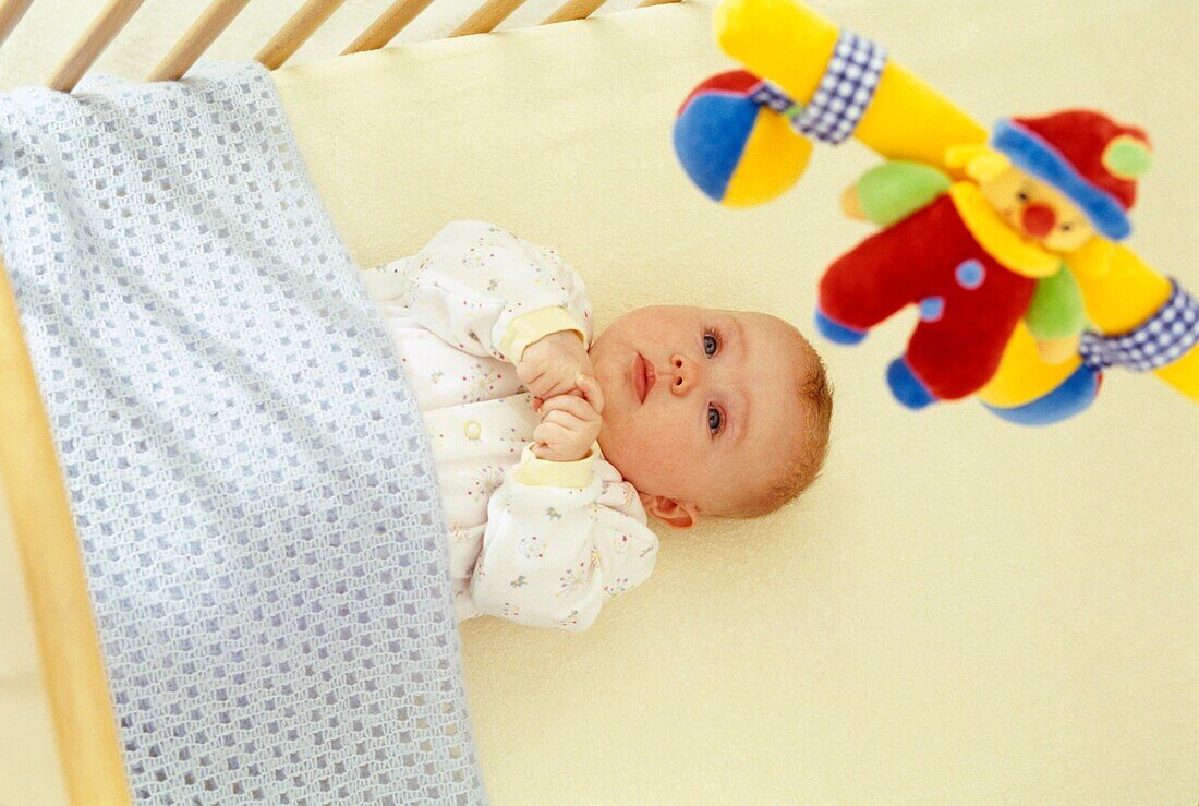 Baby in a cot looking up to a mobile