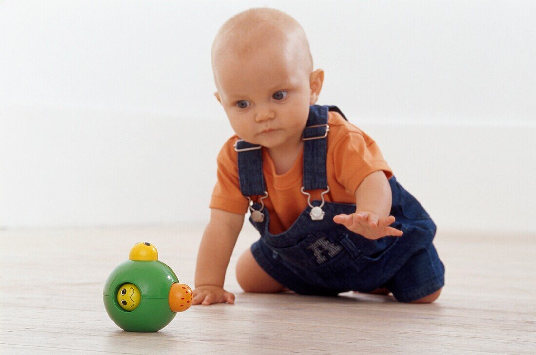 8 month old baby boy crawling on floor towards plastic toy