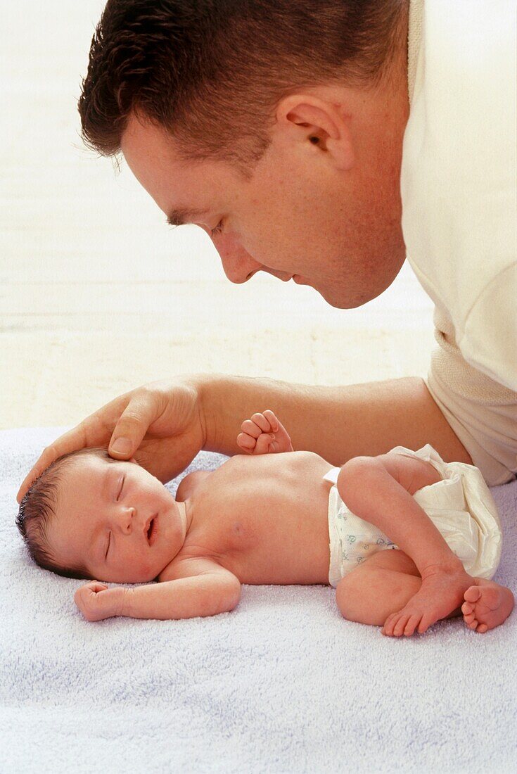 Man looking over newborn baby lying on towel