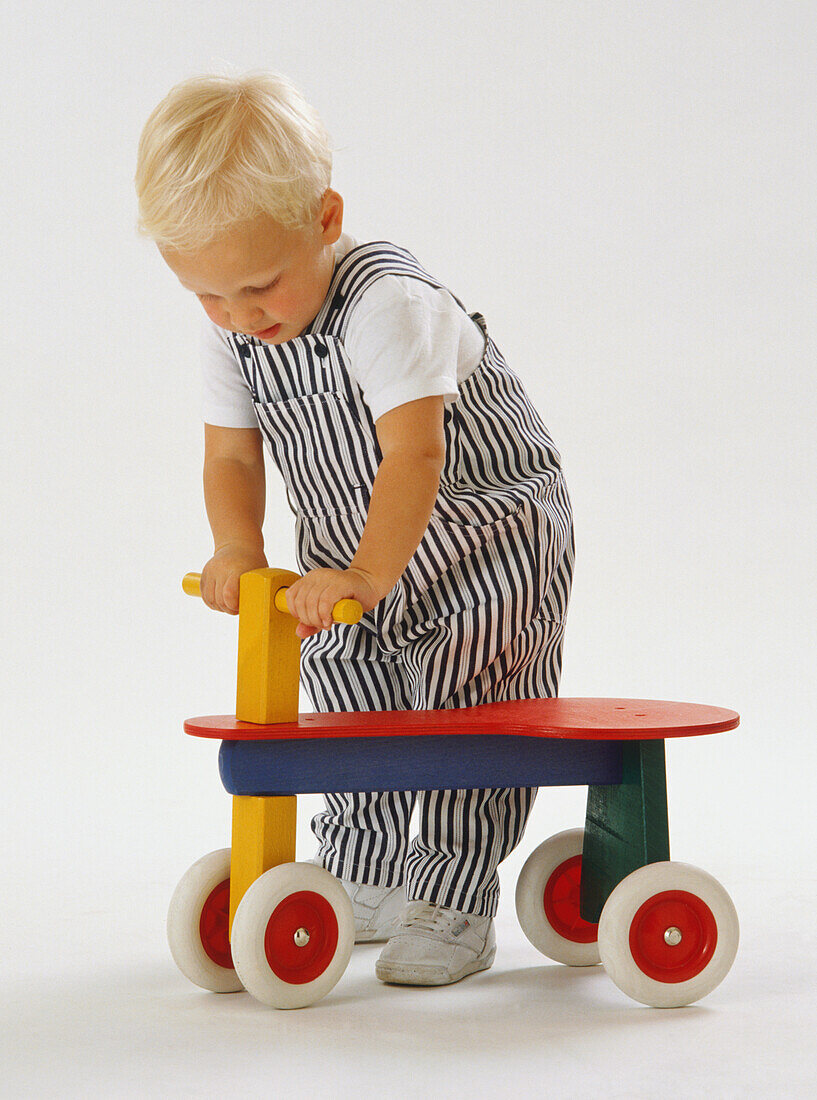Toddler holding handlebars of wooden toy tricycle
