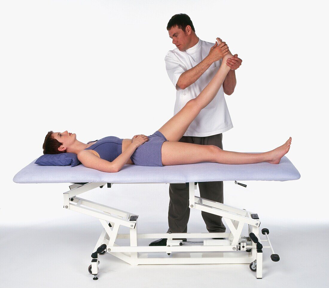 Osteopath raising leg of patient lying on back on table