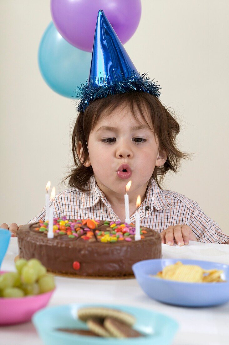 Boy wearing party hat blowing out candles on birthday cake