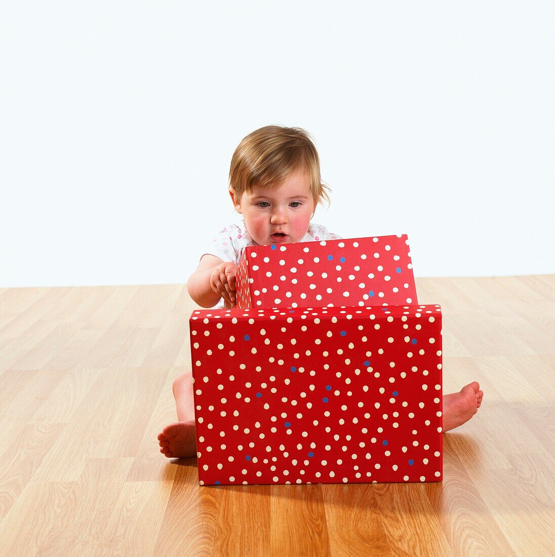 Baby girl sitting on wooden floor looking inside a box