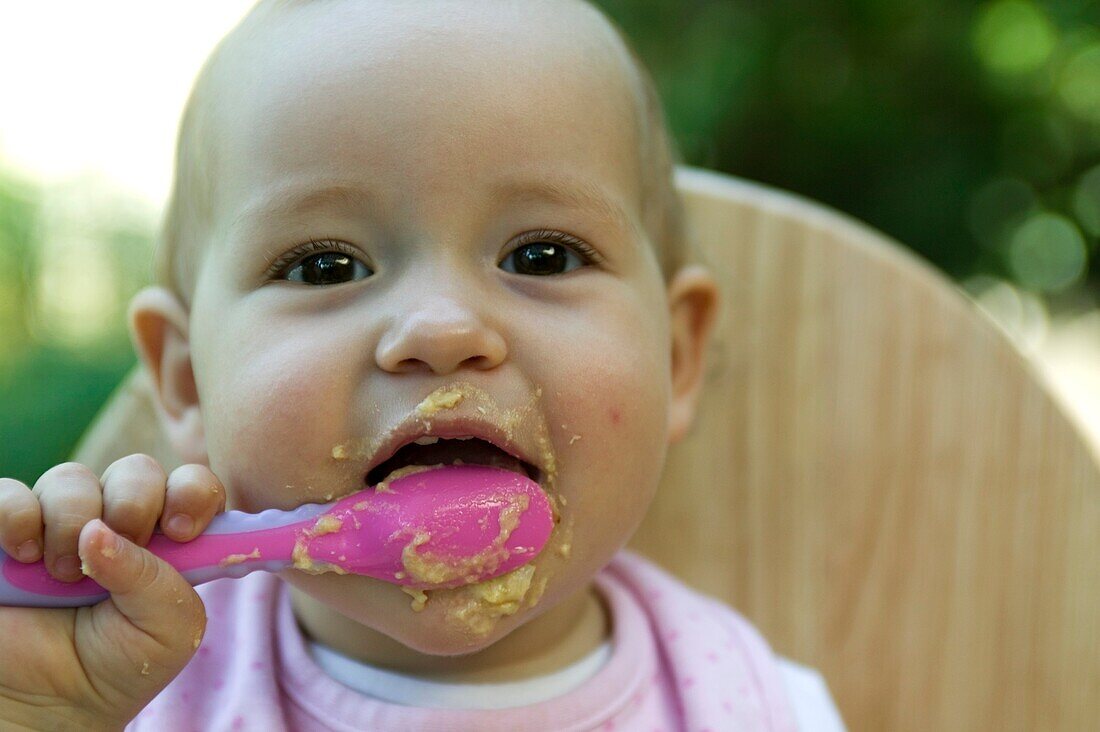 Baby girl holding spoon of baby food to her mouth