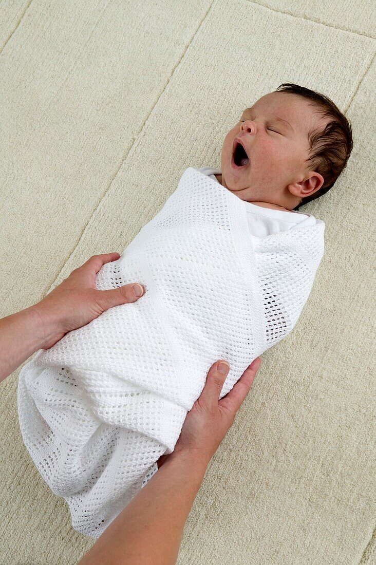 Woman's hands holding swaddled yawning baby boy