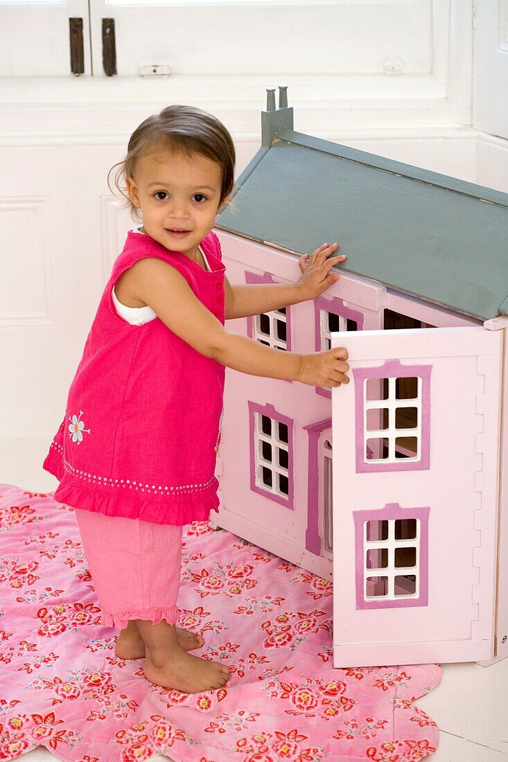 Girl in pink clothes opening door to doll's house