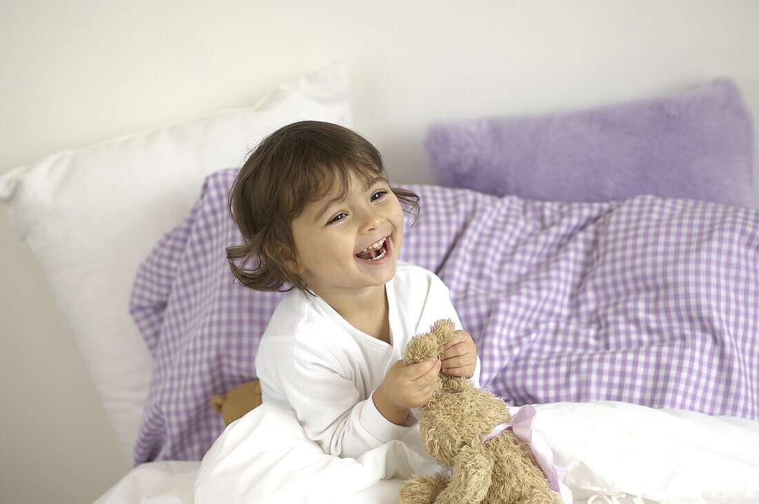 Smiling girl pulling ears of toy rabbit in bed