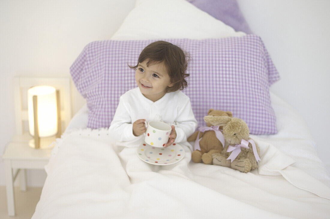Girl in pyjamas sitting up in bed holding cup and saucer