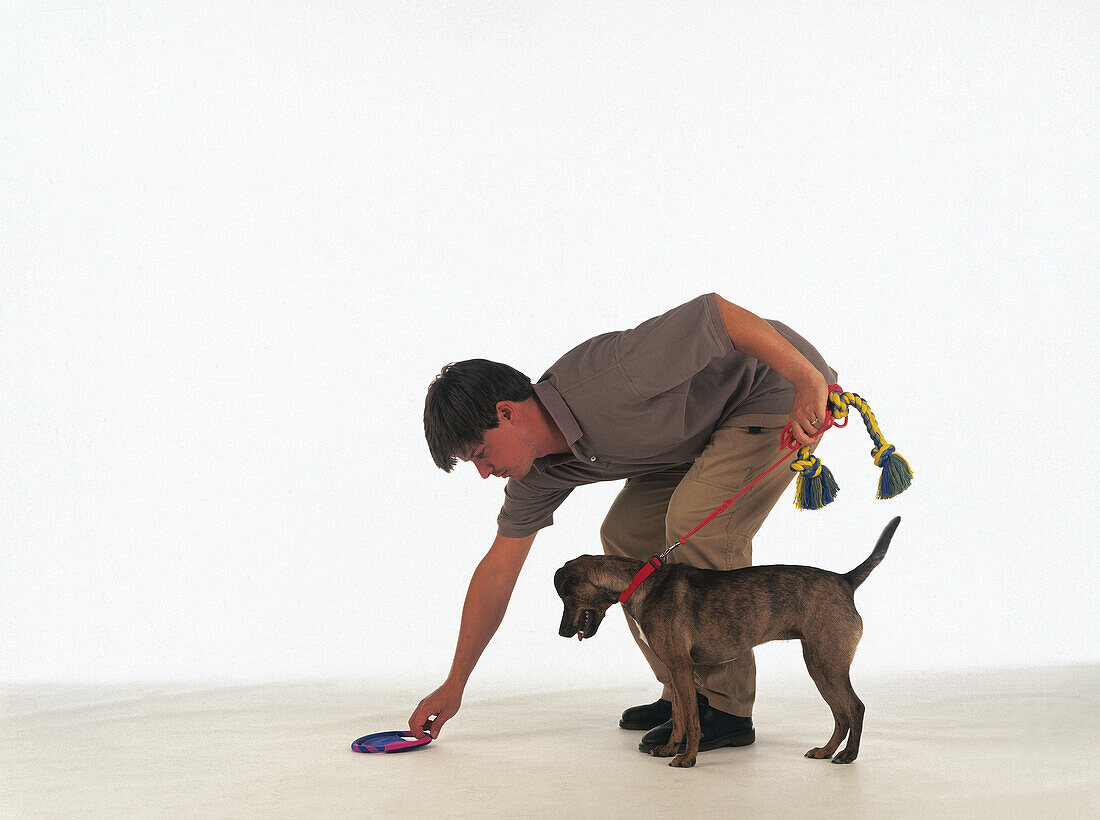 Man placing toy on the ground with dog held back on a leash