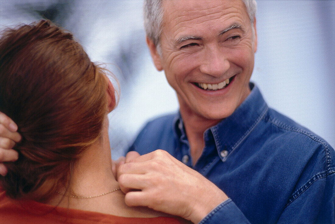 Smiling man holding a golden necklace around woman's neck