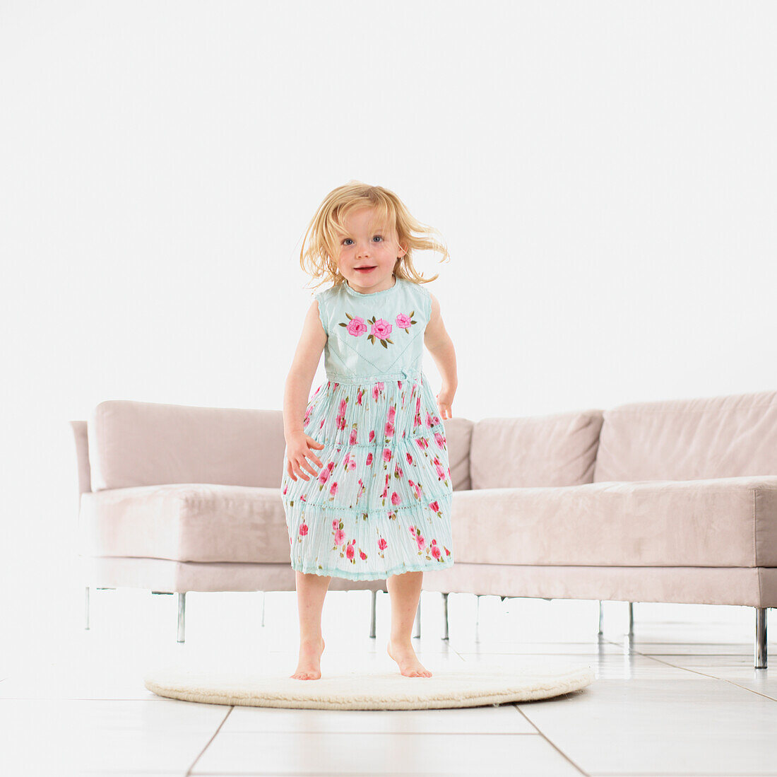 Girl jumping up from a rug in a living room with a sofa