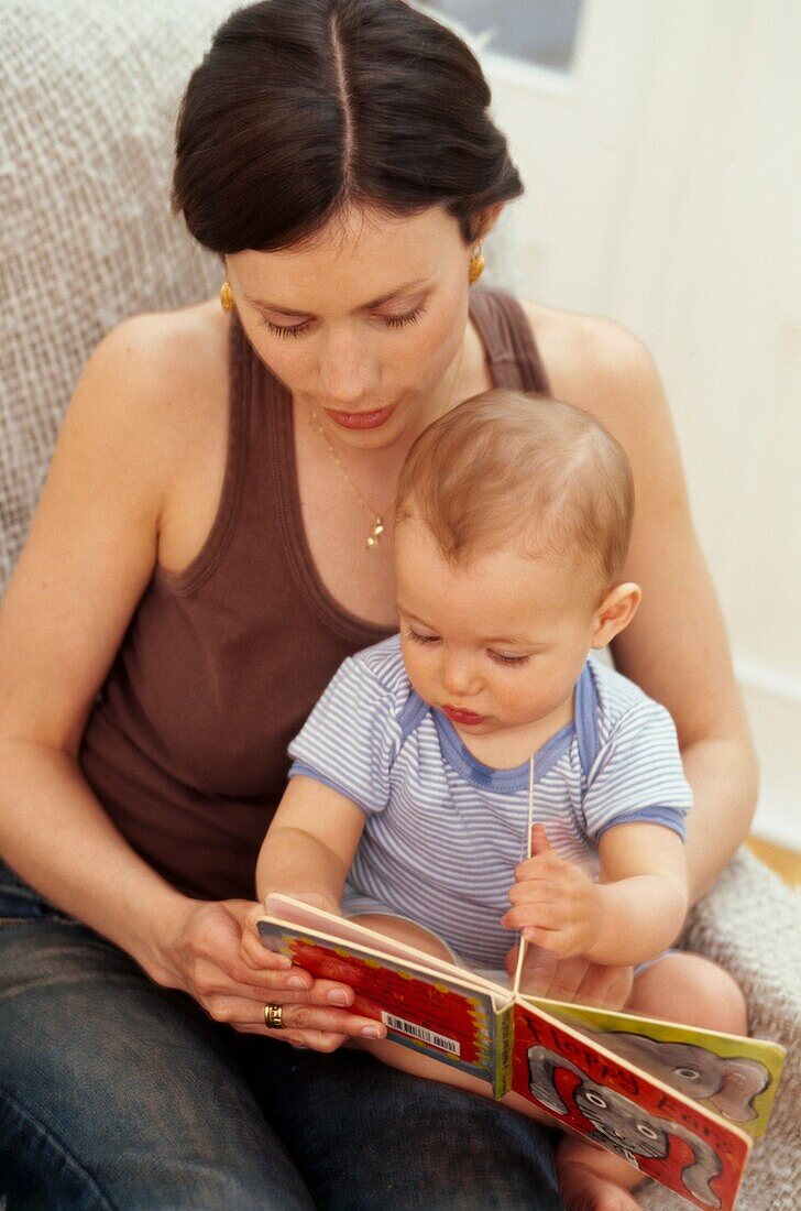 Woman with baby boy on her lap, looking at a board book