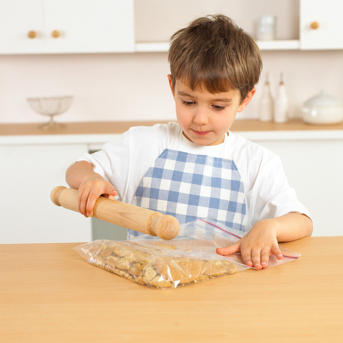 Boy holding rolling pin above bag of biscuits