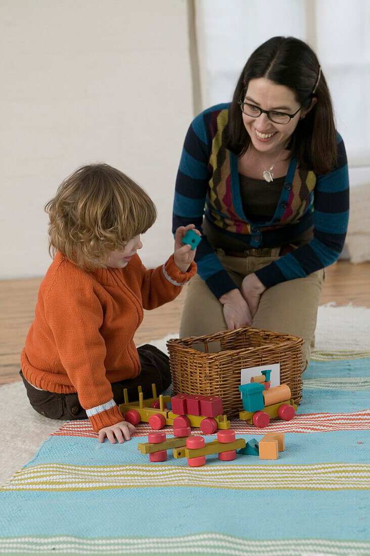 Woman smiling at a boy raising blue toy block over a basket