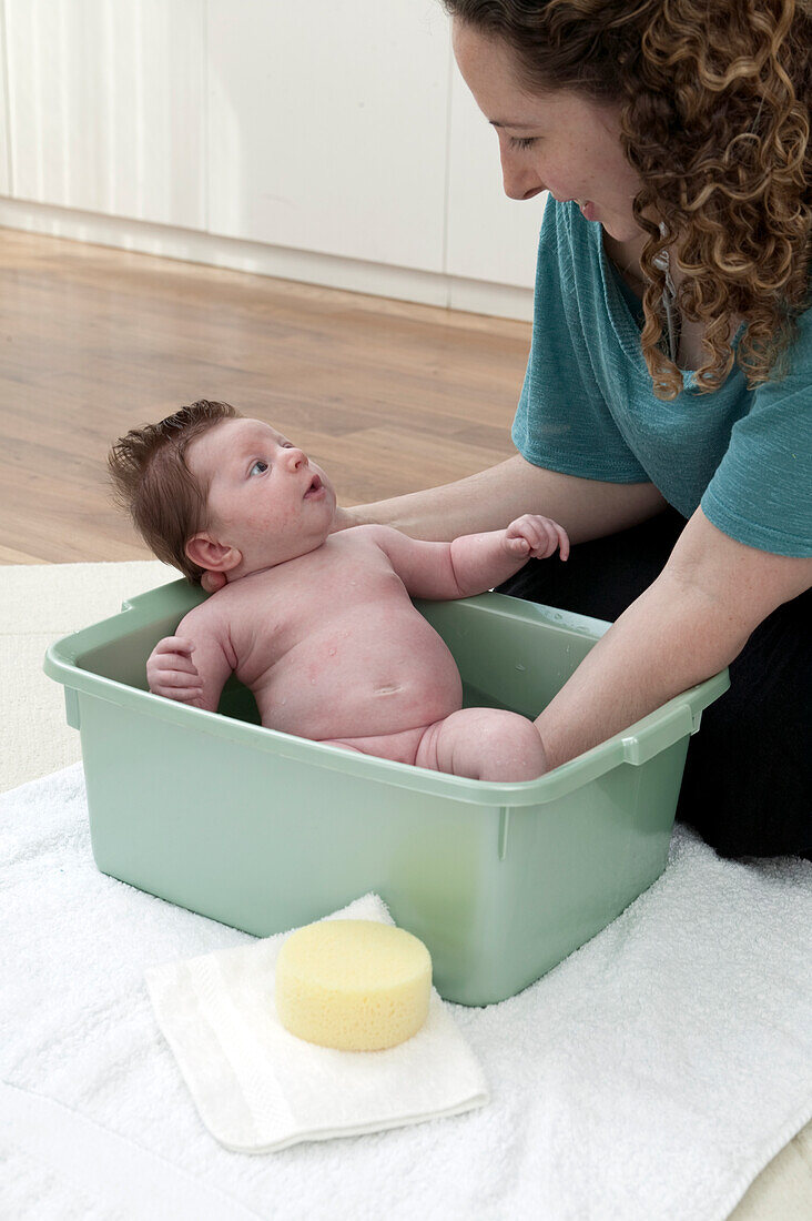 Woman holding baby in plastic green baby bath