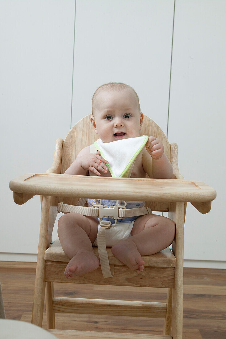Baby boy sitting in highchair holding a napkin
