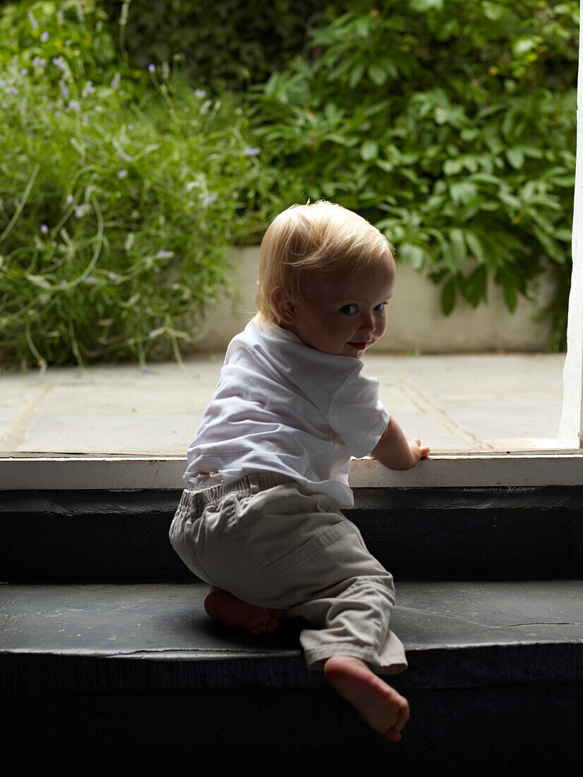 Baby boy climbing steps to patio