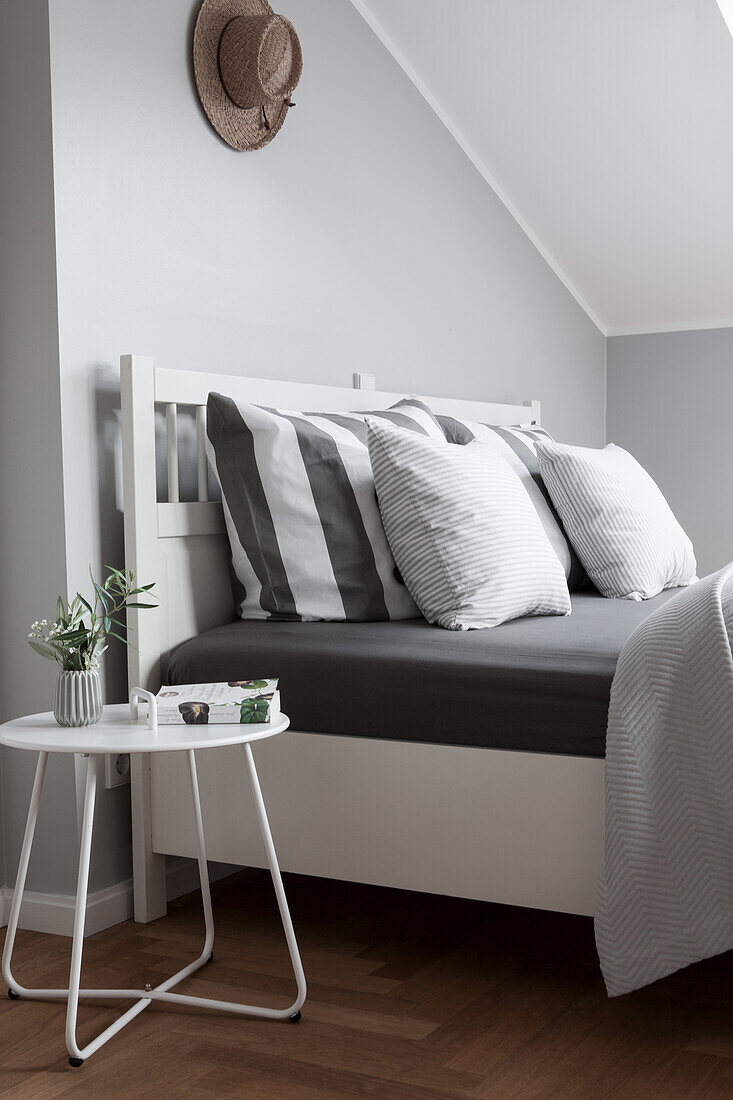 Dainty bedside table next to double bed with pillows in attic room