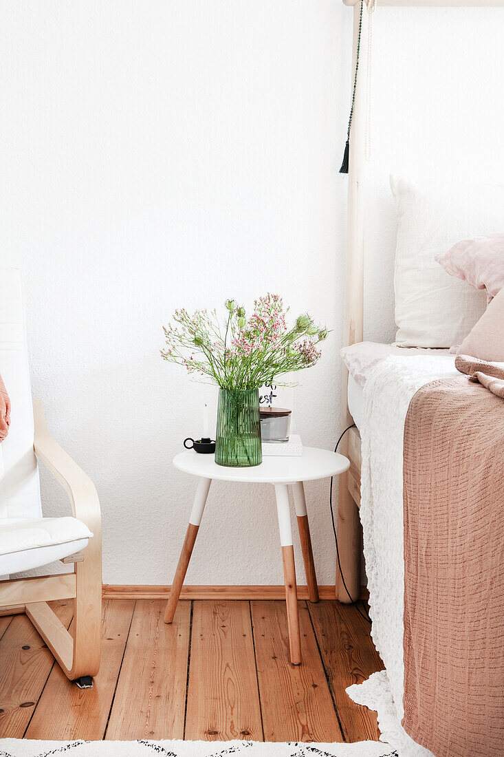 Hocker als Nachttisch zwischen Bett und Sessel in hellem Schlafzimmer