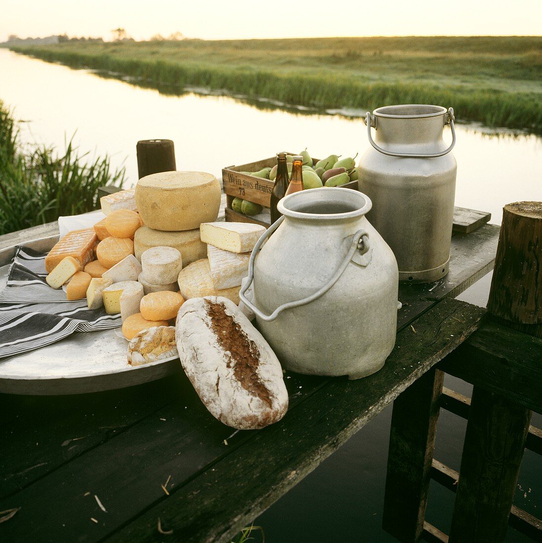 Raw-milk cheese still life with milk cans on river landing pier